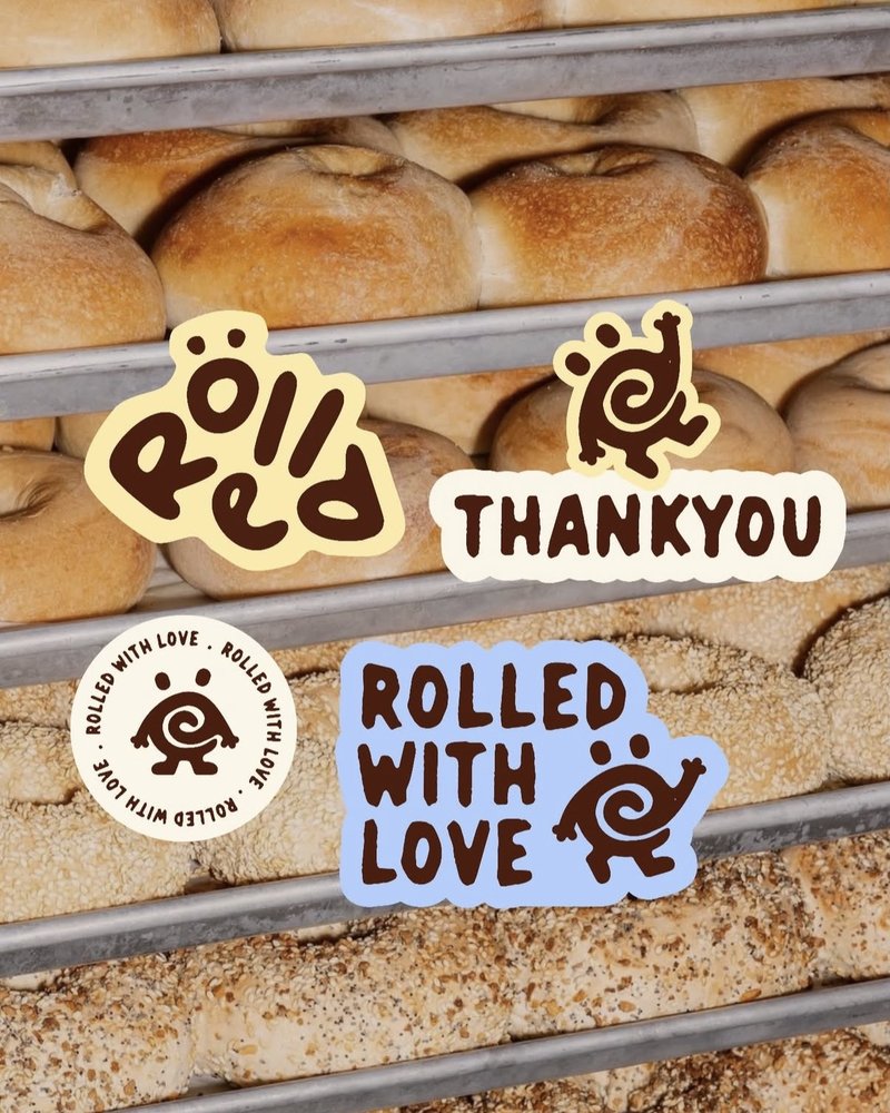 Sticker sheet applied above a bakery rack of fresh bagels, including a Rolled with Love badge
